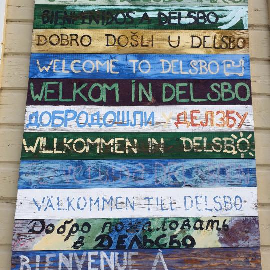 Skylt med "Välkommen till Delsbo" på flera språk