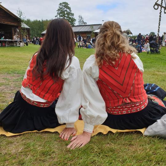 Två kvinnor klädda i Delsbodräkt som sitter på en filt