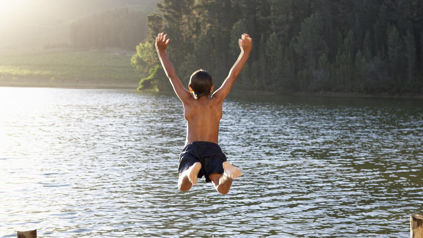 Barn hoppar i sjö från brygga